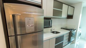 A modern kitchen with a stainless steel refrigerator, a microwave, a sink, and a stove. - PFino 206 - Apto Alto Padrão (Bombinhas)