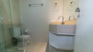 A compact bathroom with a glass shower enclosure, a toilet, and a sink with a marble countertop. - PFino 206 - Apto Alto Padrão (Bombinhas)