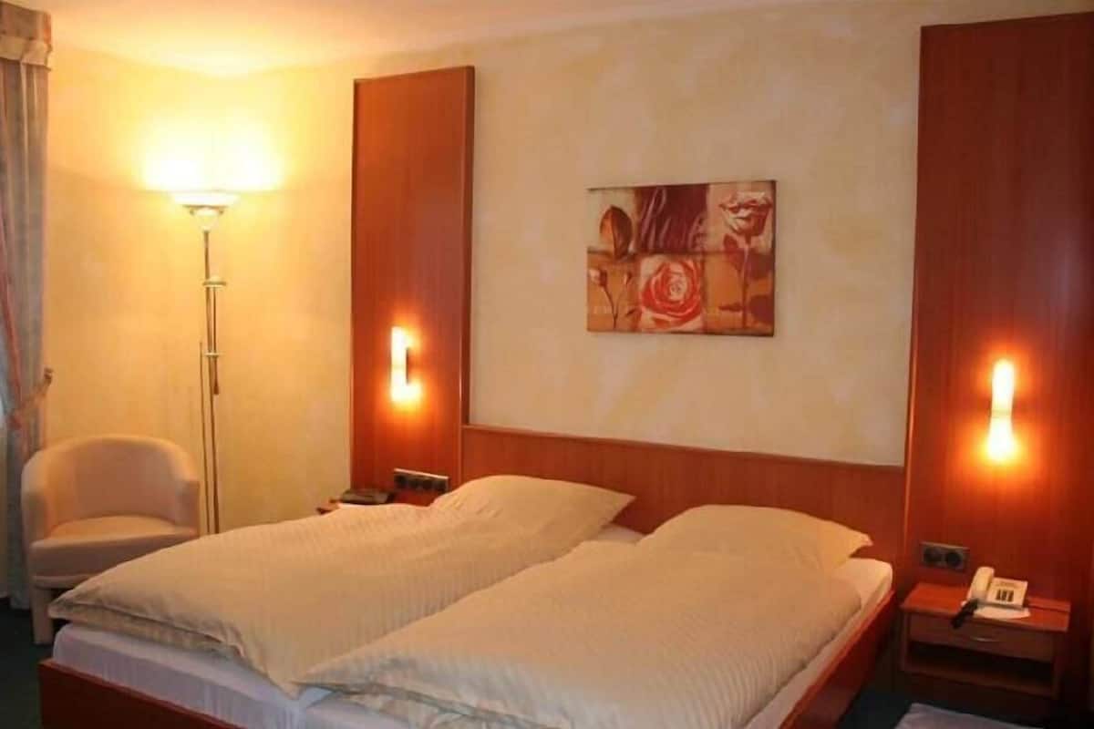 Une chambre d’hôtel avec deux lits, une chaise, une lampe sur pied et un tableau au mur.