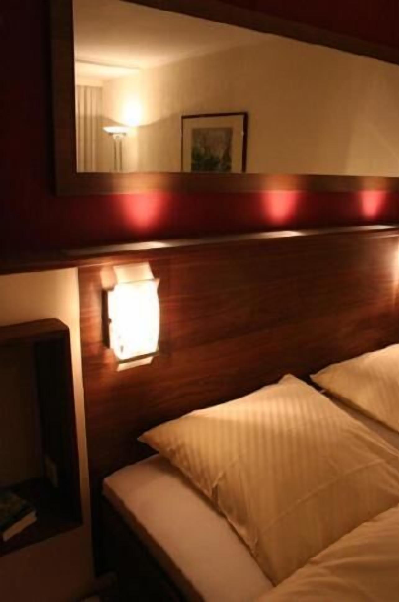 Ein Hotelzimmer mit Holz-Kopfteil, einer Nachttischlampe und einem Bett mit weißer Bettwäsche.