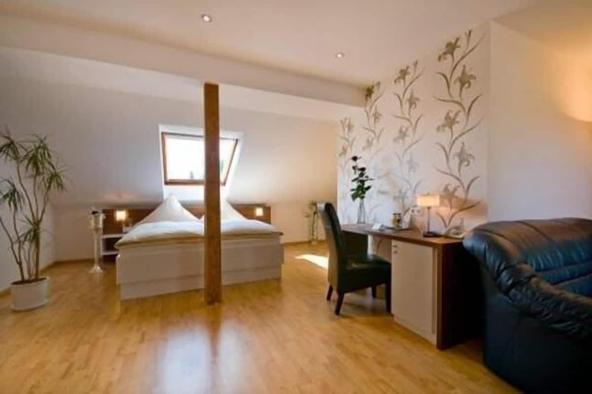 Une chambre à coucher avec un lit, un bureau, une chaise, un canapé et une plante en pot.