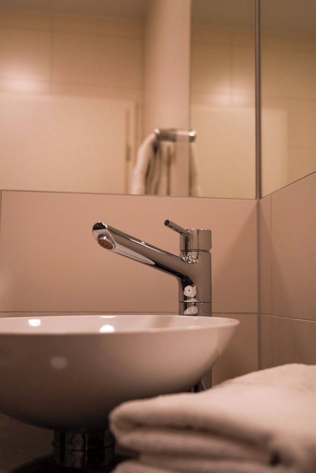 Een badkamer met een wit wastafel, een moderne kraan en een zichtbare douchezone op de achtergrond.
