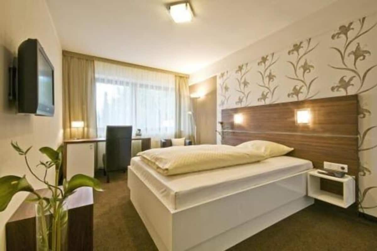 Une chambre d’hôtel comprenant un lit, une table de chevet, une télévision, un bureau, une chaise et un mur décoratif.