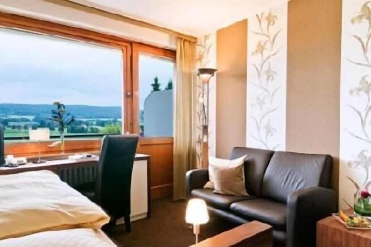 Une chambre d’hôtel équipée d’un lit, d’un bureau, d’une chaise, d’un canapé, d’une télévision et d’une fenêtre donnant sur un paysage agréable.