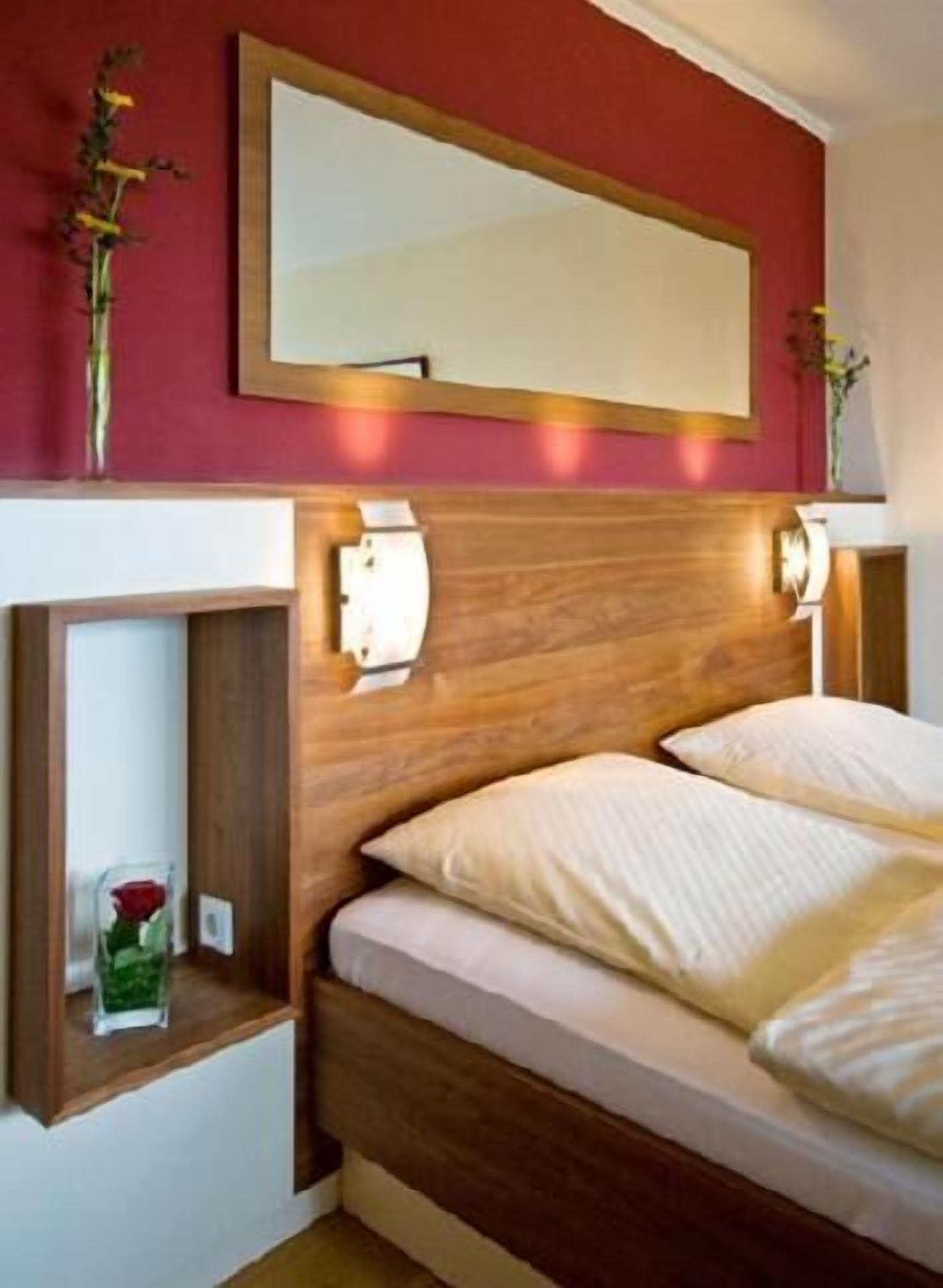 A bedroom with a wooden headboard, a bedside table with a vase of flowers, and a mirror above the bed.