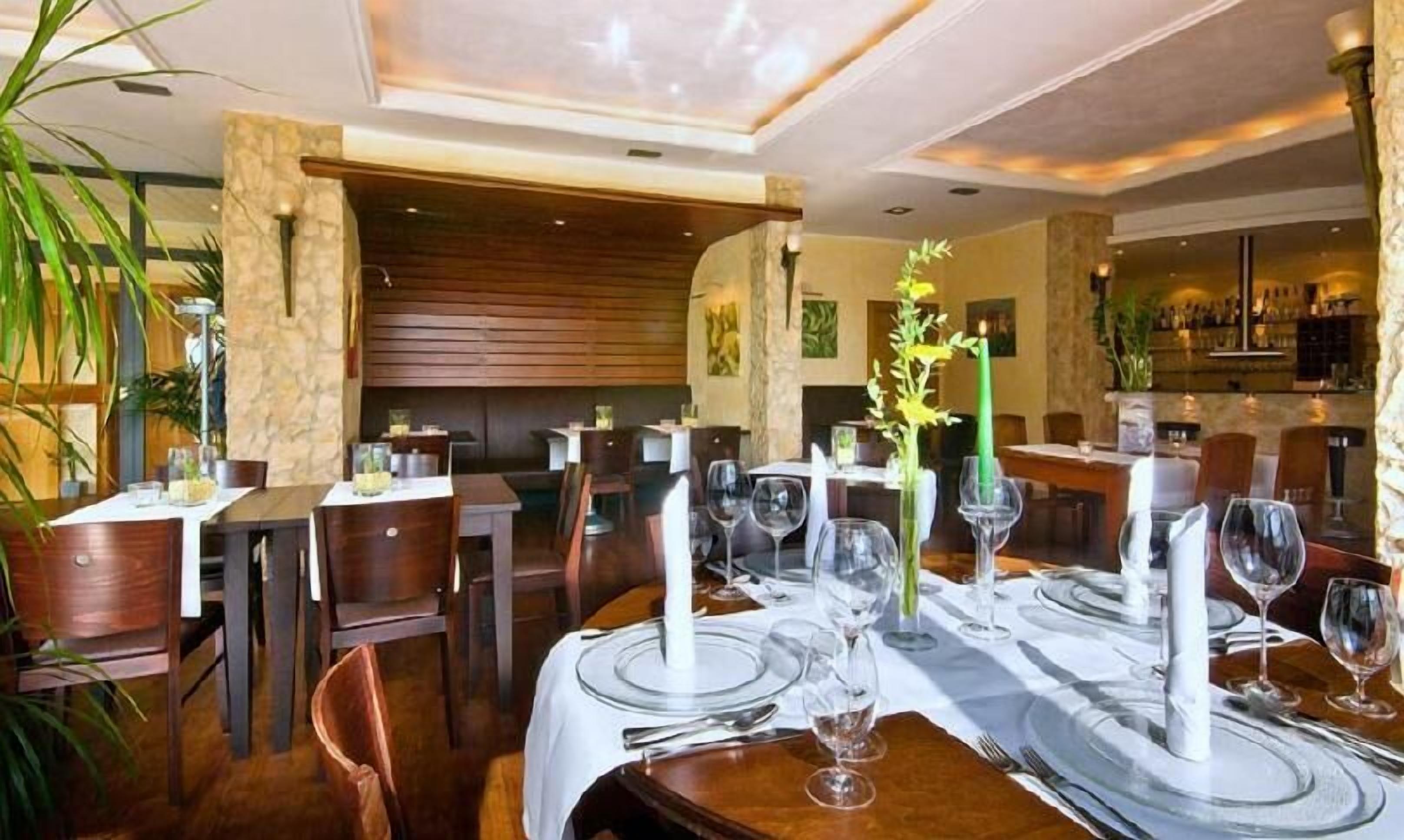 Ein Restaurant mit Holztischen und -stühlen, weißen Tischdecken und grünen Kerzen.