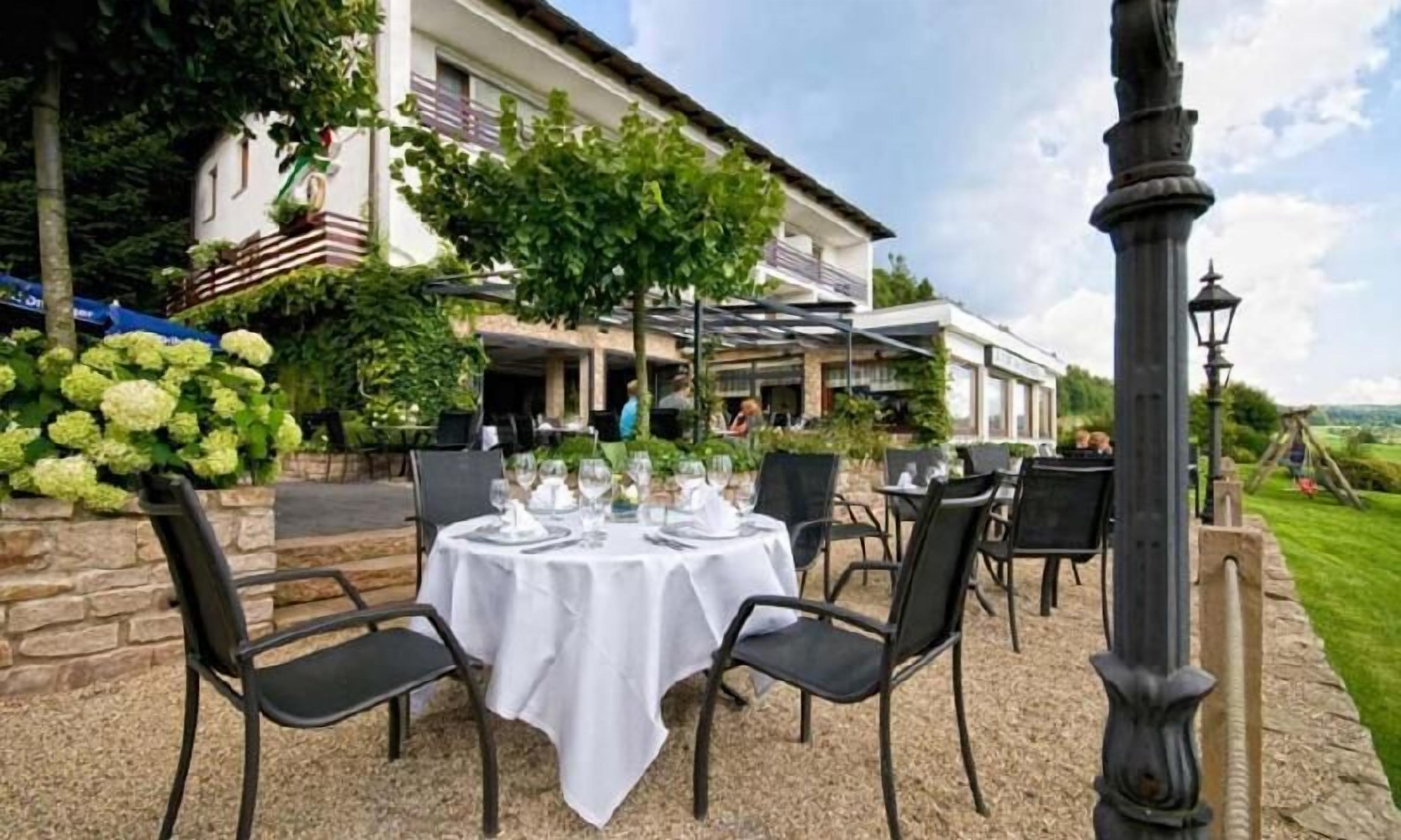 Un espace de restauration en plein air avec des tables dressées pour les clients, entouré de verdure et avec un bâtiment en arrière-plan.