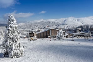 Estância de esqui coberta de neve, com um grande chalé, pistas de esqui e montanhas ao fundo.