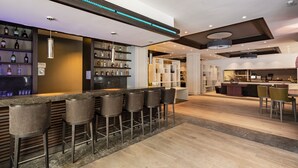 Zona de bar moderna con una barra alargada, varios taburetes y estantes llenos de botellas.