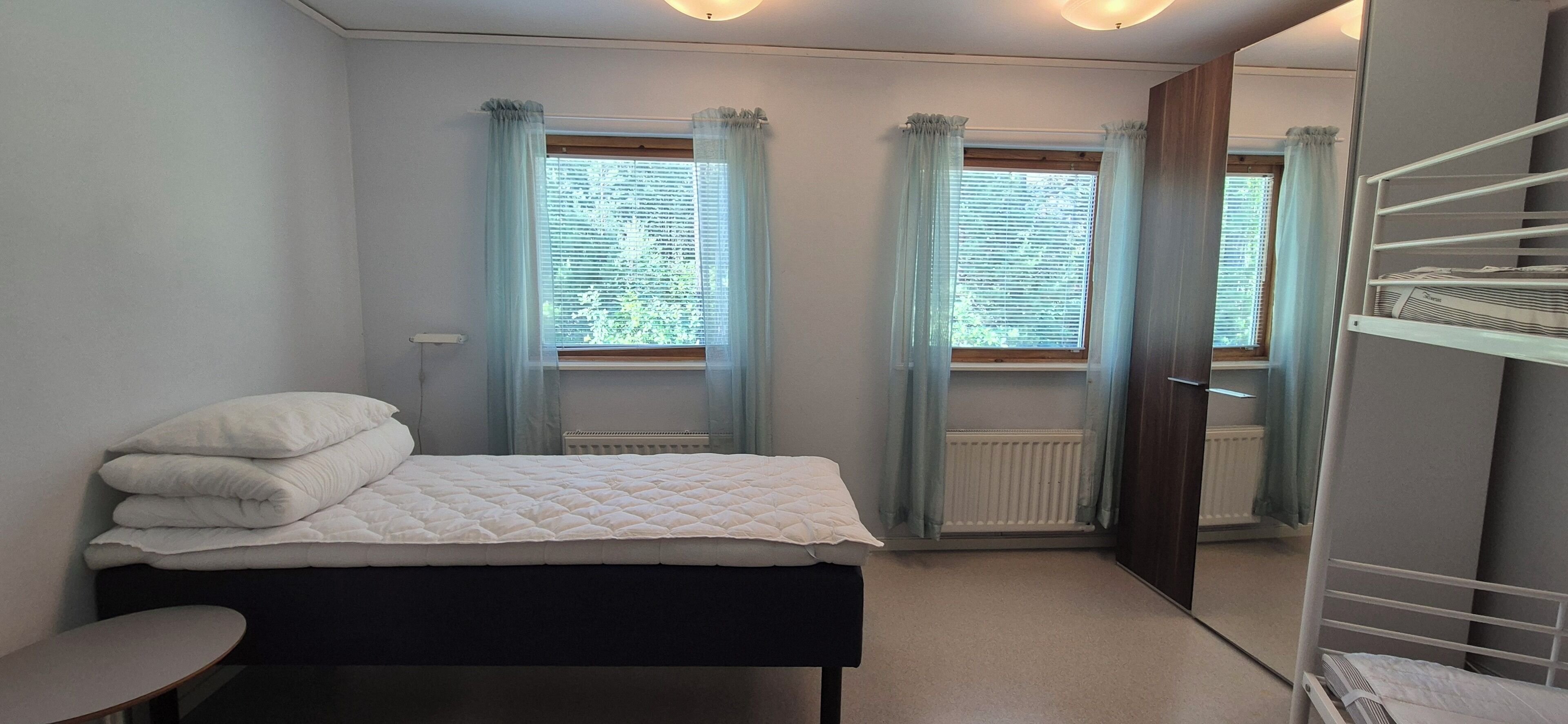Un dormitorio con cama, mesita de noche, radiador y ventana con cortinas.