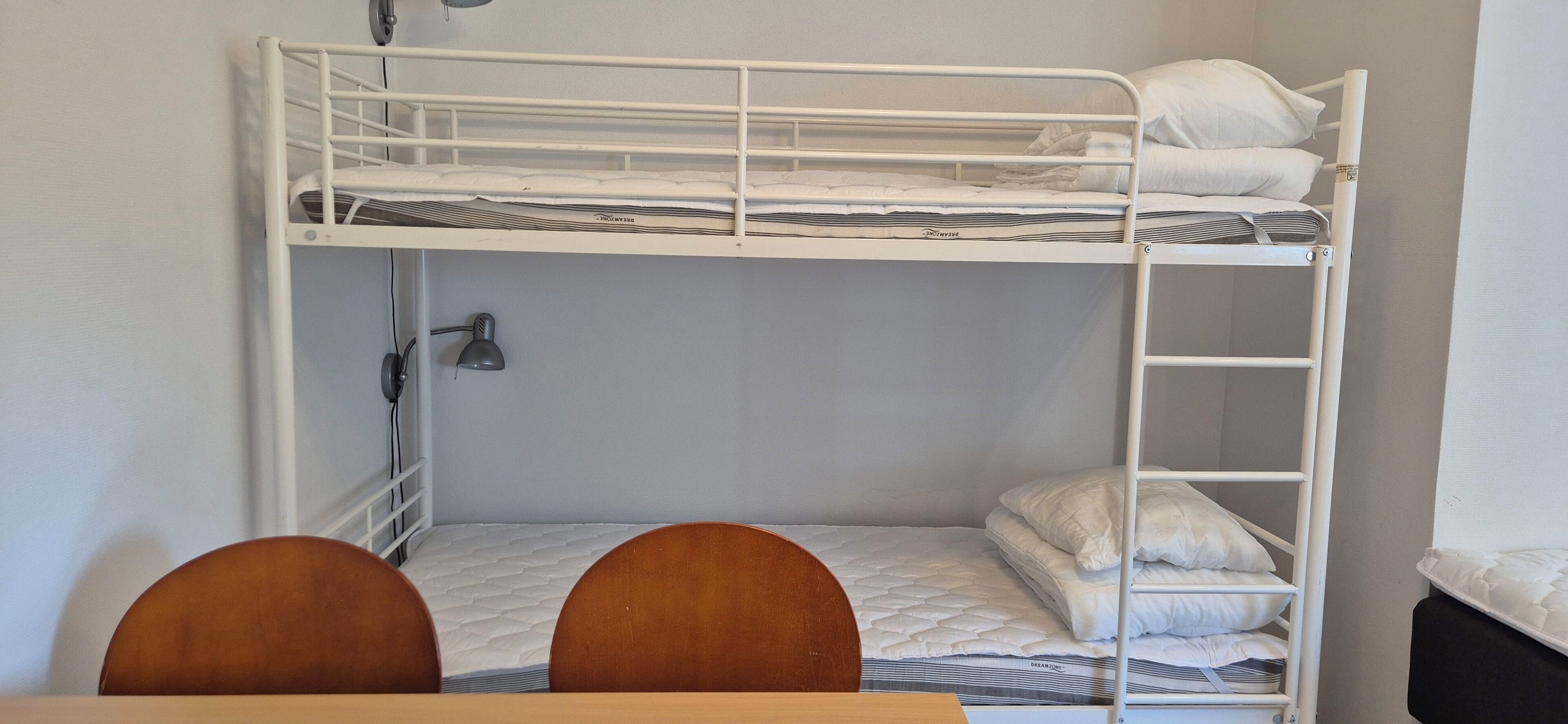 A bunk bed with two levels, a desk with a chair, and a lamp.