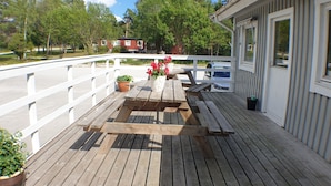 Een houten terras met een witte reling, een picknicktafel en potplanten.