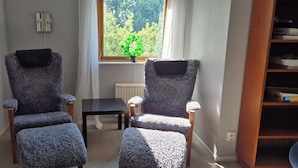 Twee fauteuils met een tafeltje ertussen, een raam met uitzicht op bomen en een radiator aan de muur.