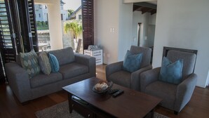 A living room with two grey sofas, a coffee table, and a view of a house through open shutters. - 10 Martingale (Knysna)