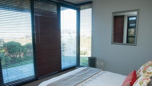A bedroom with a bed, a window with blinds, a radiator, and a mirror on the wall. - 10 Martingale (Knysna)