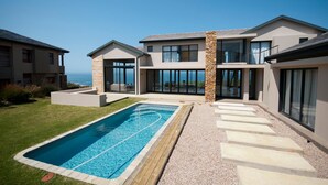 Une maison moderne à deux étages, dotée d’une piscine, de grandes baies vitrées et d’un mur d’accent en pierre.