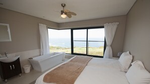 Une chambre avec un grand lit, une baignoire, un lavabo et une vue sur l’océan.