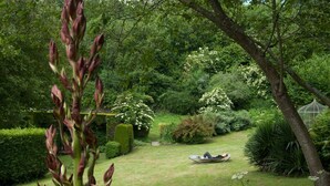 A well-maintained garden with a boat on the grass, surrounded by various plants and trees. - Le Logis du Jerzual (Dinan)
