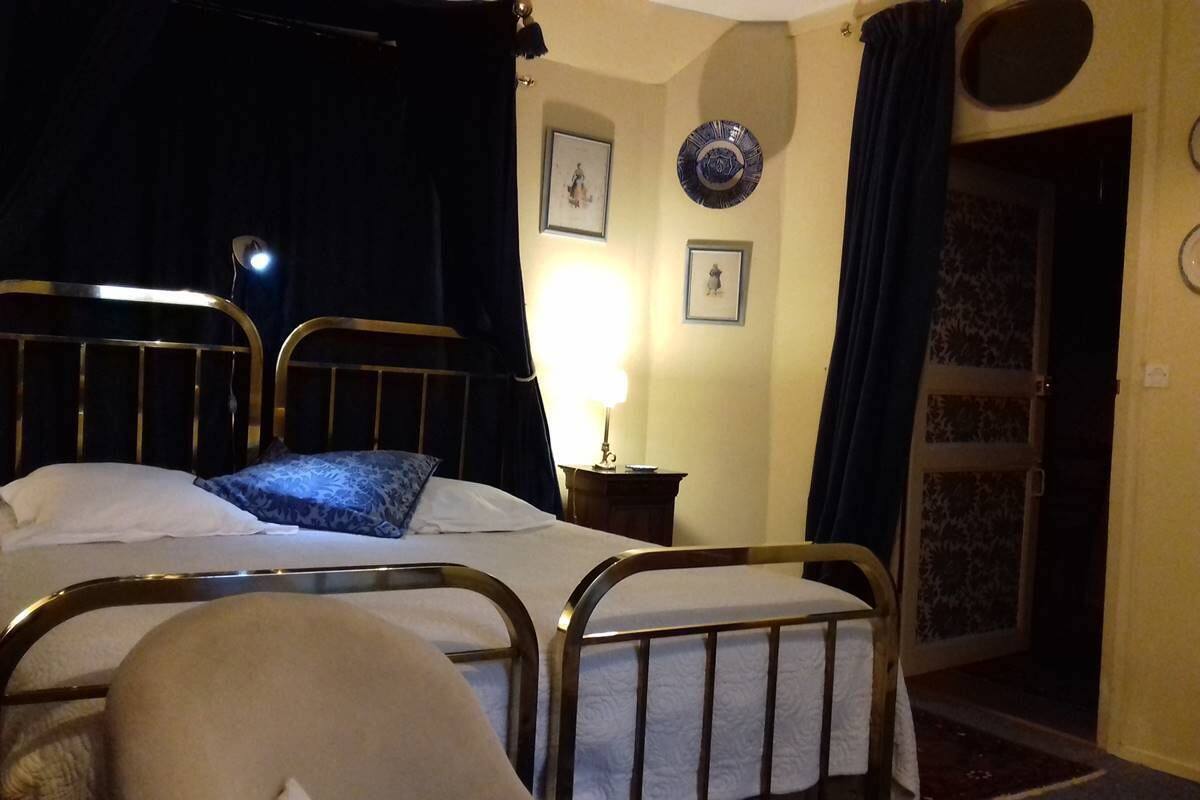 A hotel room with two beds, a chair, a lamp, and a door leading to another room.