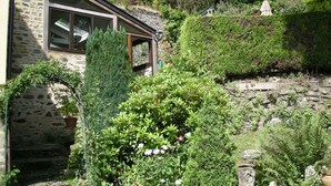 A stone building with a large window, surrounded by dense greenery and a stone wall. - Le Logis du Jerzual (Dinan)