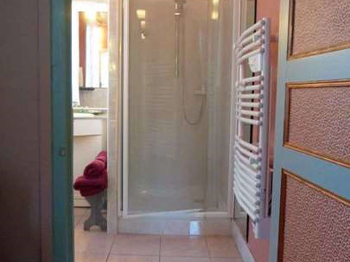 A bathroom with a glass shower enclosure, a white radiator, and a red towel on a stool.