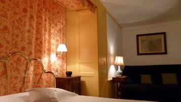 A hotel room with a bed, two bedside tables with lamps, a dark-colored sofa, and a floral-patterned curtain.