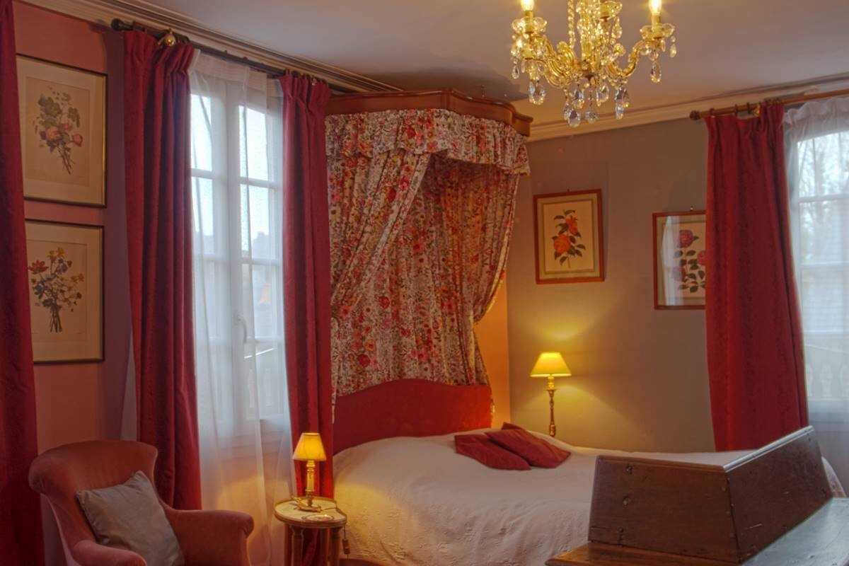 A bedroom with a bed, a chair, a table, a lamp, and a chandelier.