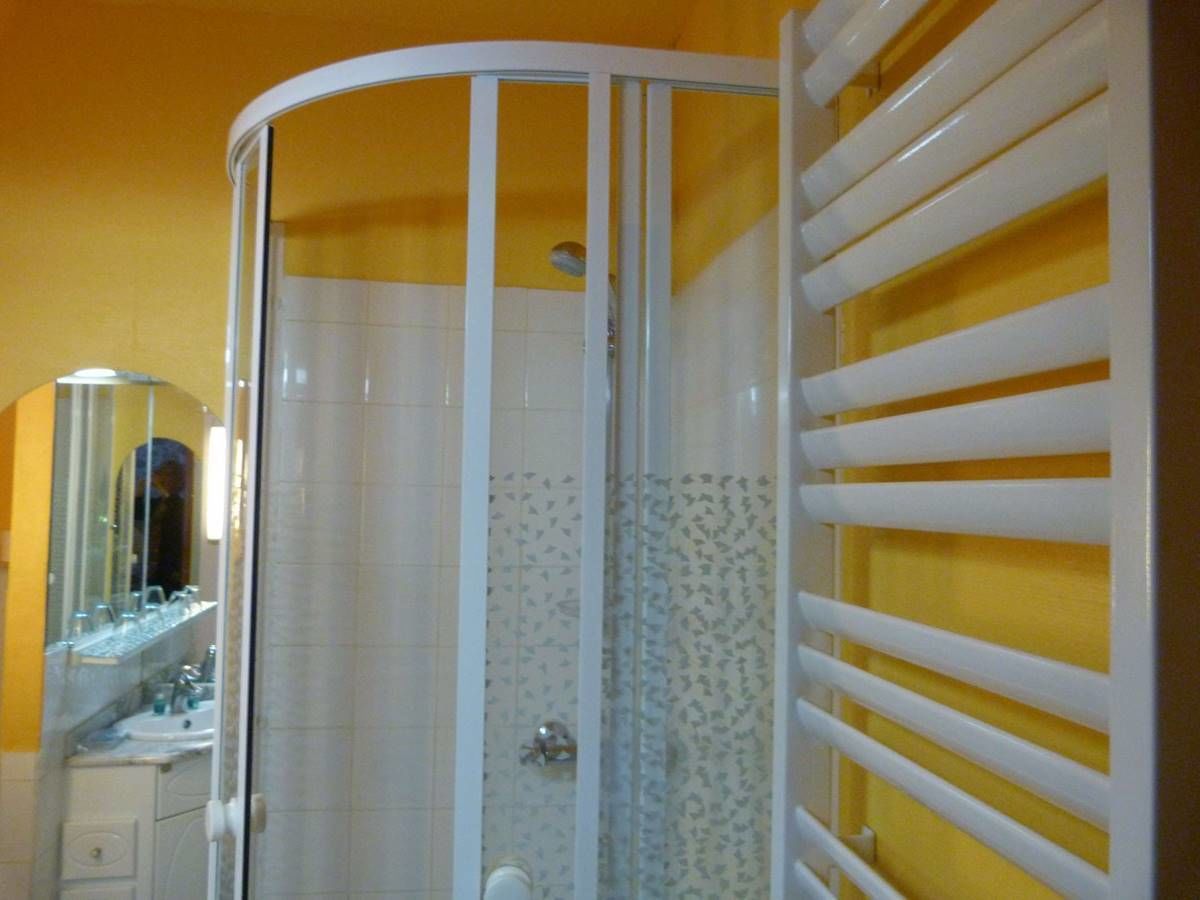 Un baño con mampara de vidrio, bañera blanca y pared amarilla.