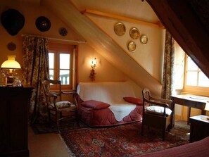 A cozy attic bedroom with a red sofa, two wooden chairs, a small table, and a decorative lamp.