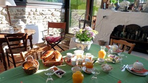 A breakfast table set with bread, butter, fruit, and beverages, surrounded by stone walls and wooden furniture. - Le Logis du Jerzual (Dinan)