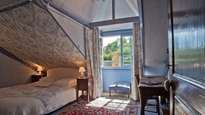 A bedroom with a bed, bedside table, lamp, and a view of greenery outside. - Le Logis du Jerzual (Dinan)