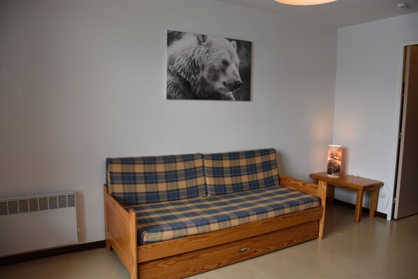 A room with a wooden sofa, a small table with a lamp, and a wall-mounted picture.