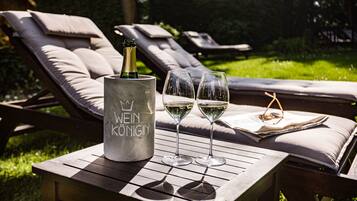 Een tafel met een wijnfles en twee glazen witte wijn, omringd door loungestoelen in een tuin.