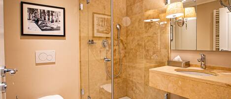 Un baño moderno con ducha envuelta en vidrio, inodoro blanco, lavabo con espejo y un cuadro en la pared.