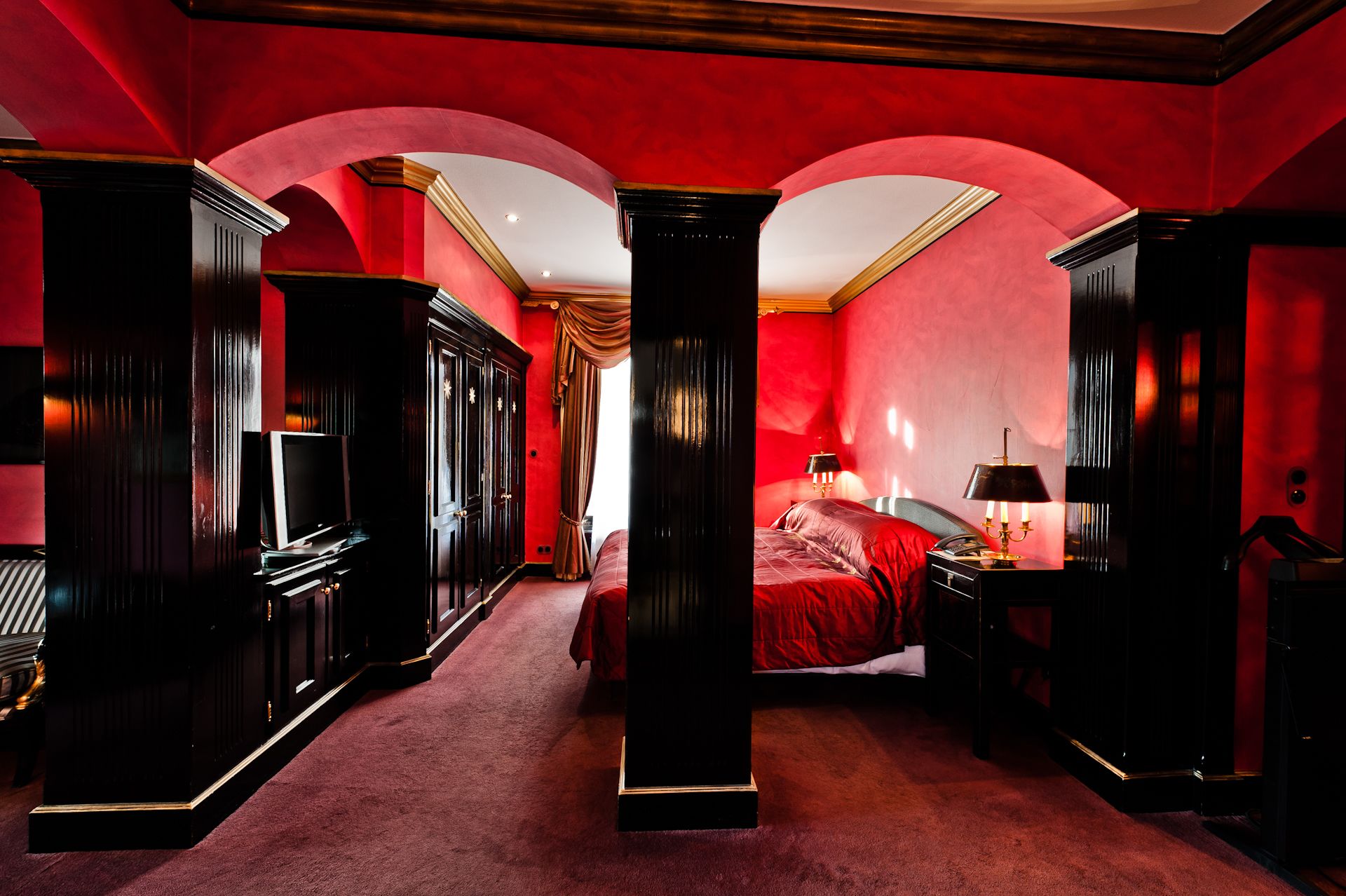 Una habitación con una pared roja, una cama, un escritorio y un armario.