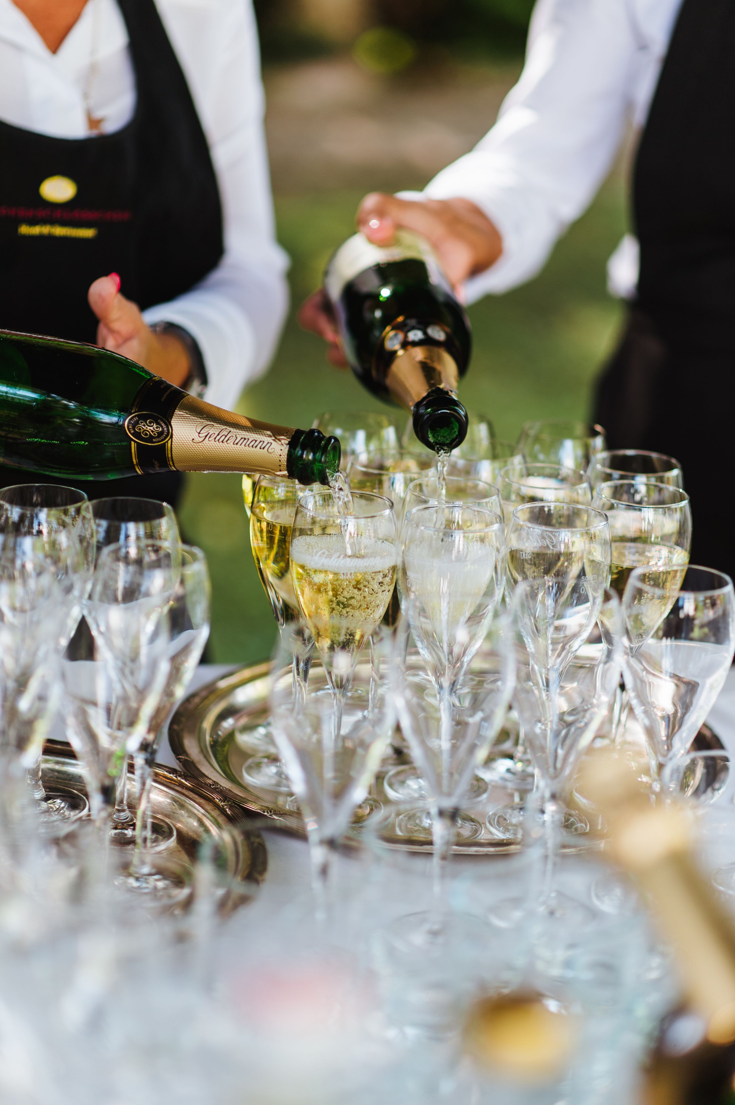 Une personne verse du champagne dans plusieurs verres disposés sur un plateau.