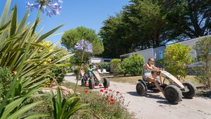 A garden with a dirt path, a trailer, and a person riding a small vehicle. - Yelloh Village La Plage (Penmarch)
