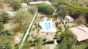 An aerial view of a property with a swimming pool, surrounded by greenery and a few buildings. - Yuna Village Garden Resort (Old-Yundum)