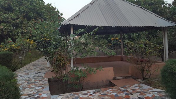 A covered outdoor area with a tiled walkway leading to a seating area surrounded by plants and trees. - Yuna Village Garden Resort (Old-Yundum)