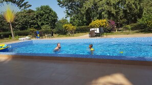 Una piscina rectangular con bordes azulejados, rodeada por una solana con mosaicos.