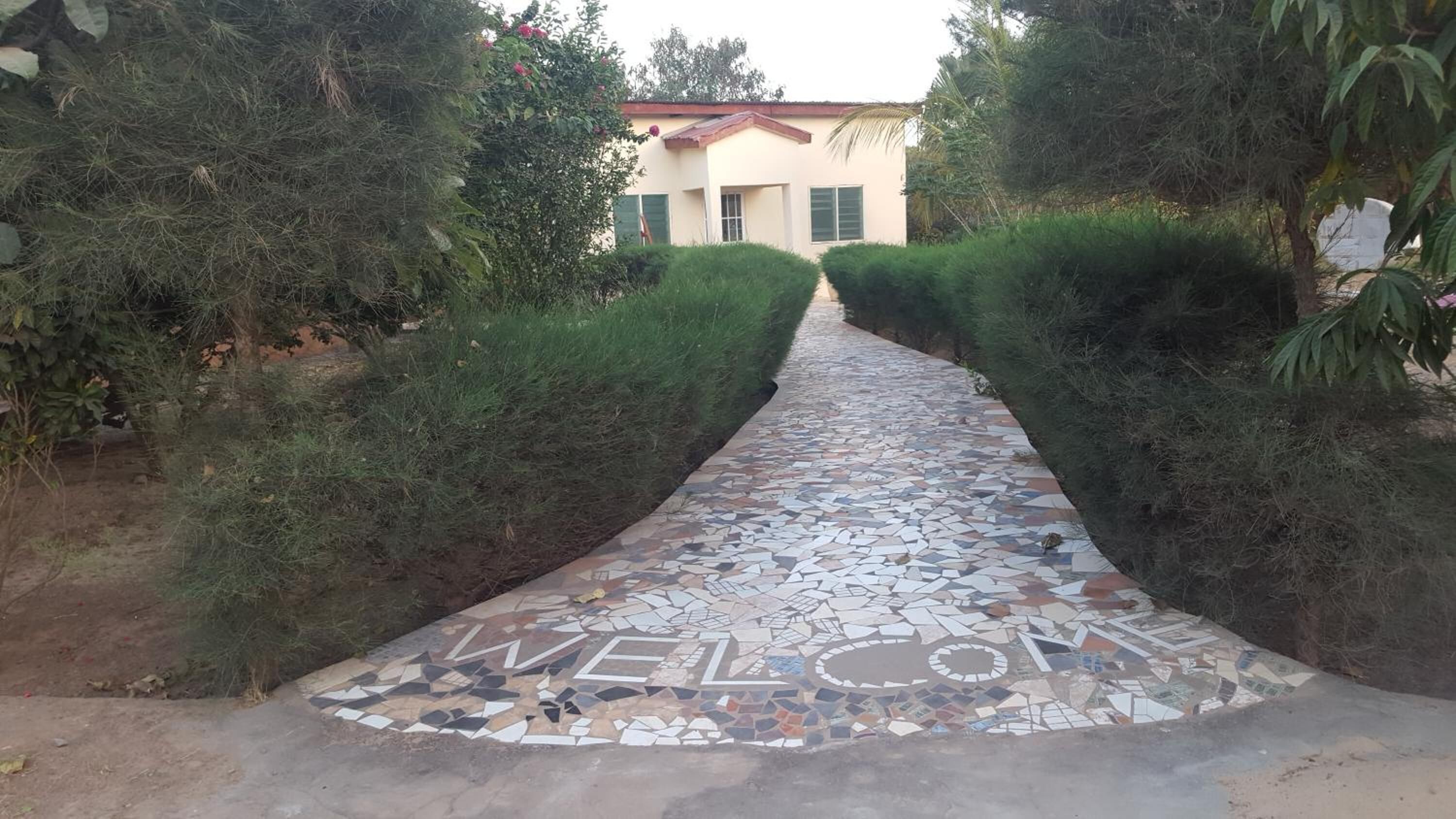 Un chemin pavé de mosaïques mène à un bâtiment doté d’un toit rouge et de volets verts.