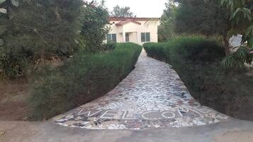 Un chemin pavé de mosaïques mène à un bâtiment doté d’un toit rouge et de volets verts.