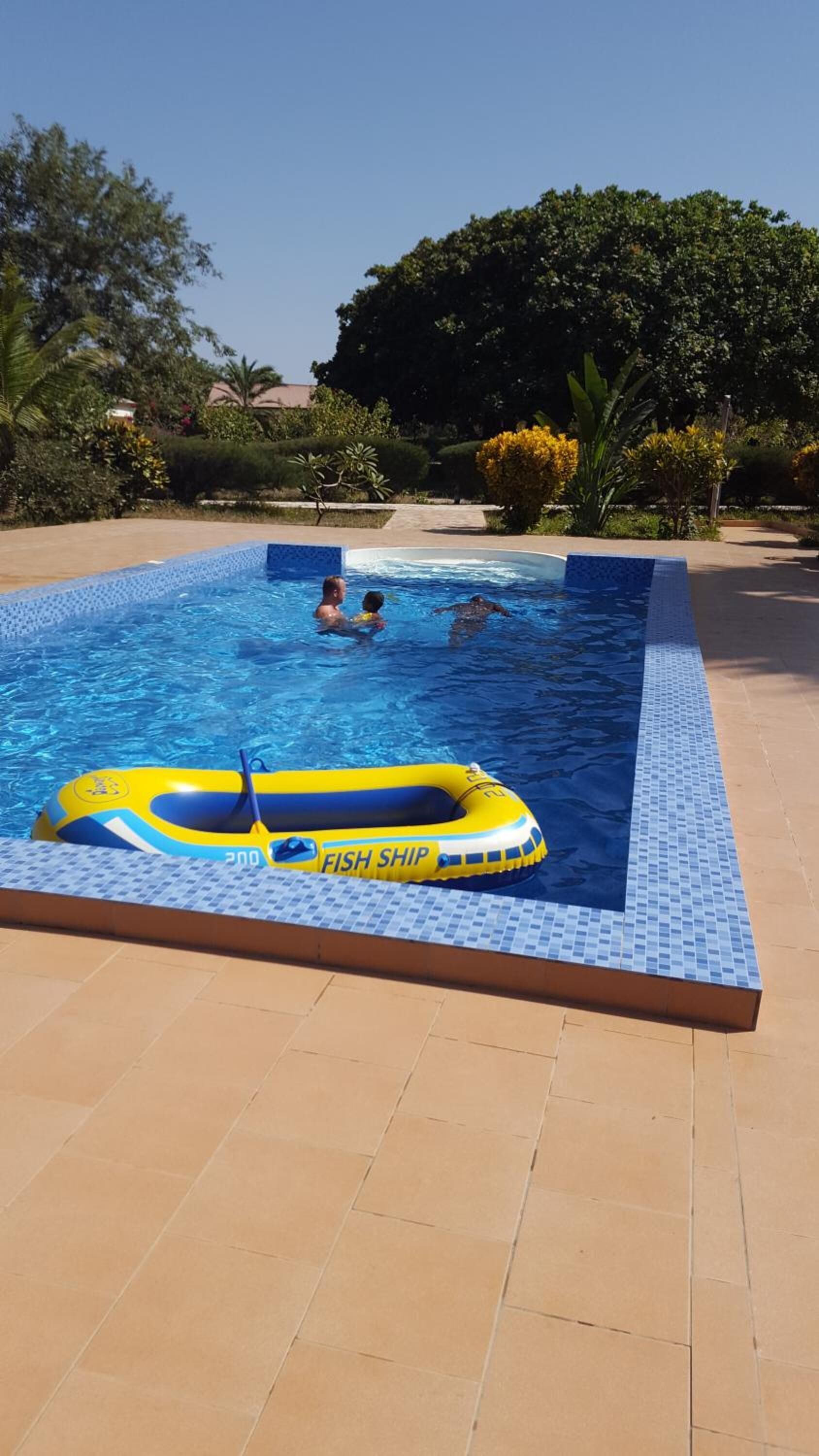 Una piscina con un bote inflable amarillo con la leyenda "FISH SHIP" y bordes de azulejos.