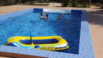 Una piscina con un bote inflable amarillo con la leyenda "FISH SHIP" y bordes de azulejos.