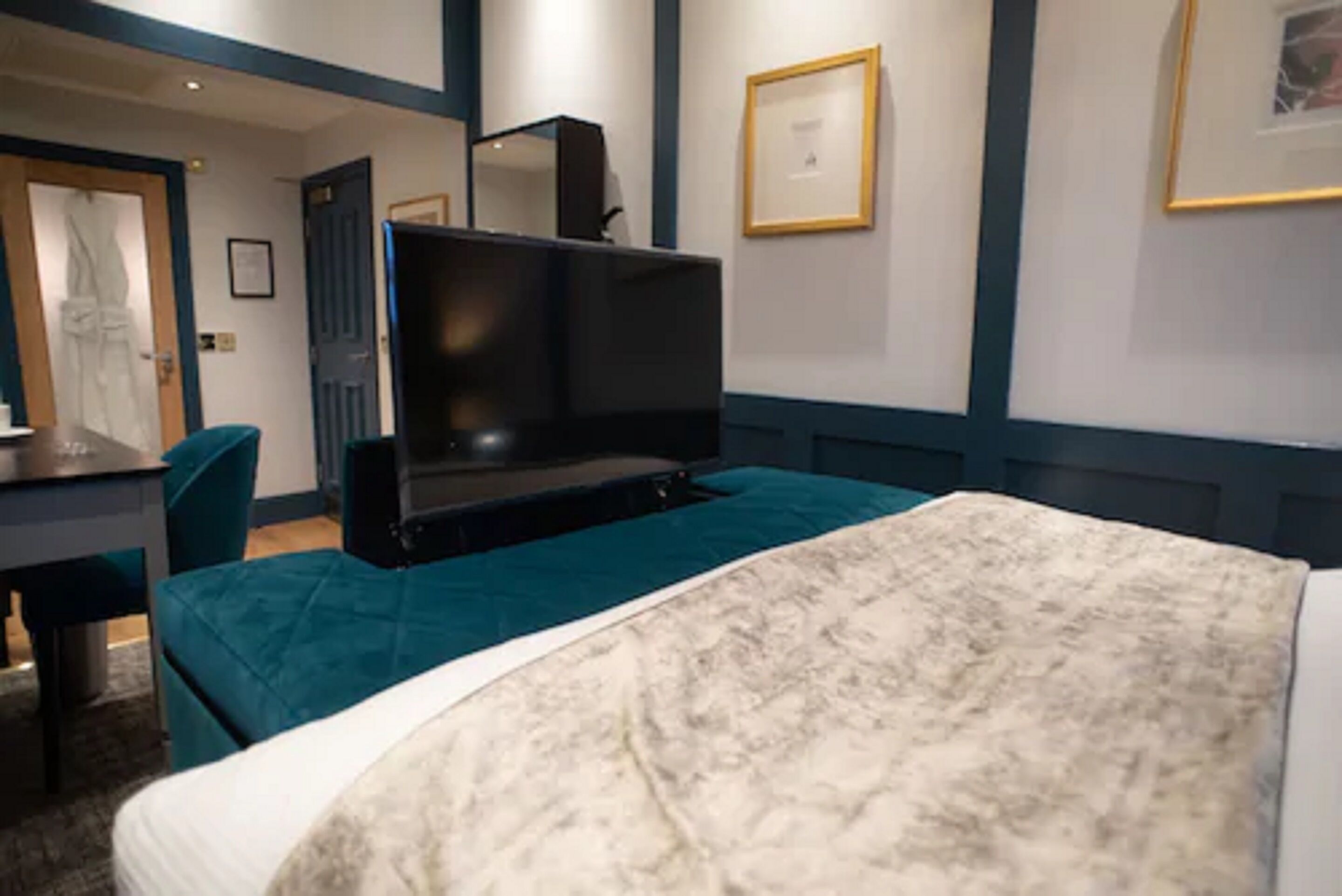 A hotel room with a bed, a desk, a chair, a television, and framed pictures on the wall.