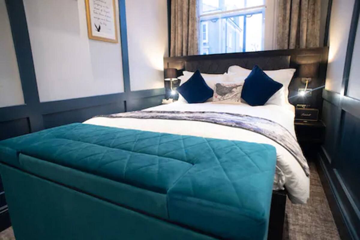 A neatly made bed with a teal quilted headboard, a wooden headboard, and two bedside lamps.