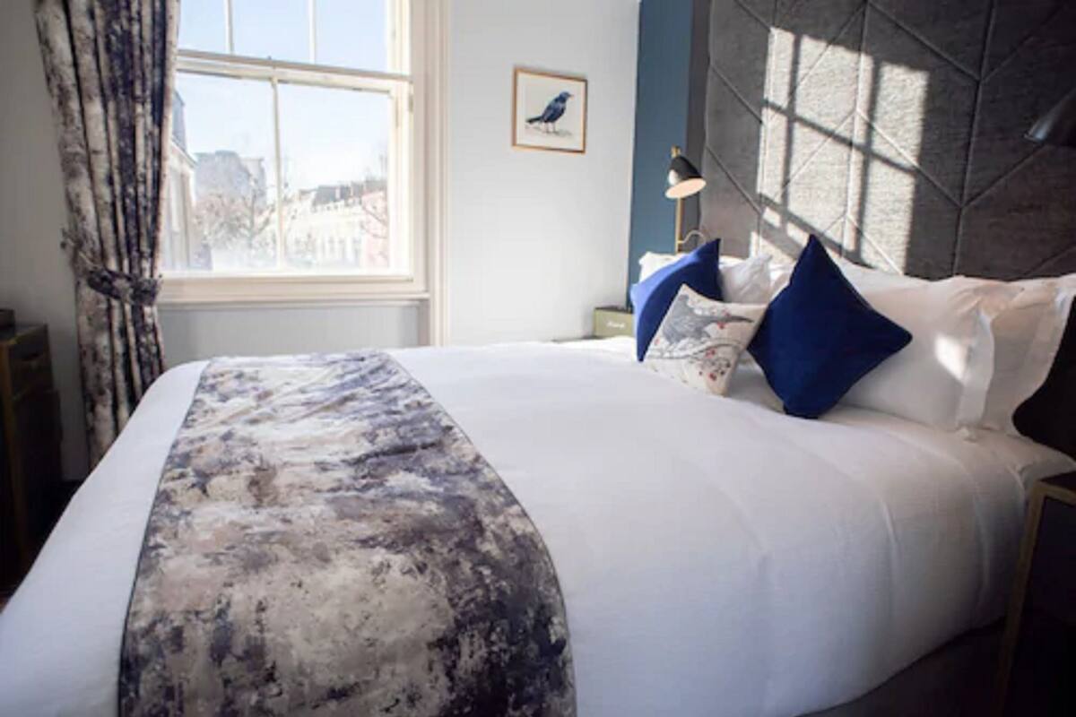A neatly made bed with a patterned throw, a framed picture on the wall, and a window with curtains.