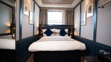 A modern hotel room with a large bed, dark blue walls, and a ceiling light fixture.
