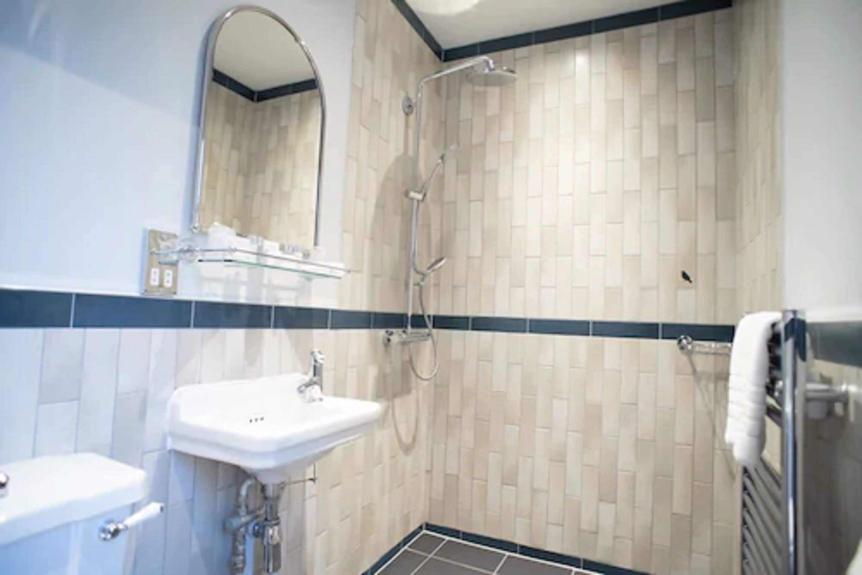 Une salle de bain avec un lavabo, un miroir, une douche et des murs carrelés.