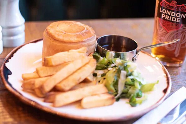 A plate with a meat pie, fries, and a salad, accompanied by a metal cup and a bottle of beer.